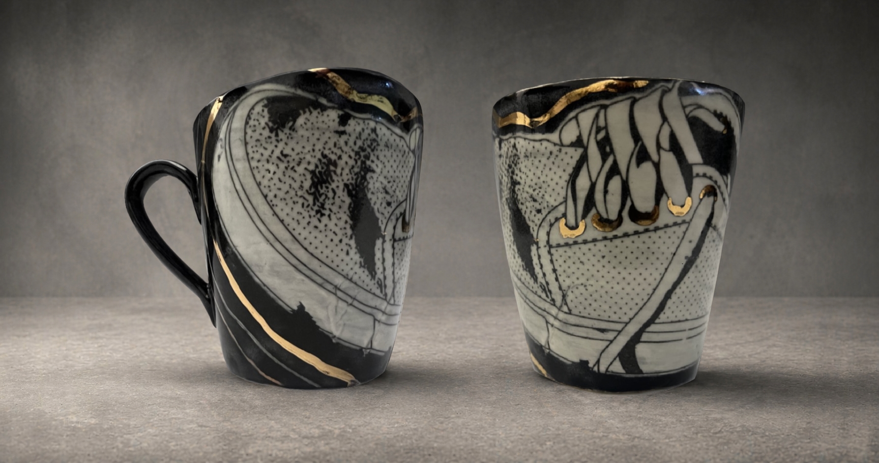 Two hand-thrown ceramic mugs, black and white with gold accents, depicting sneaker imagery